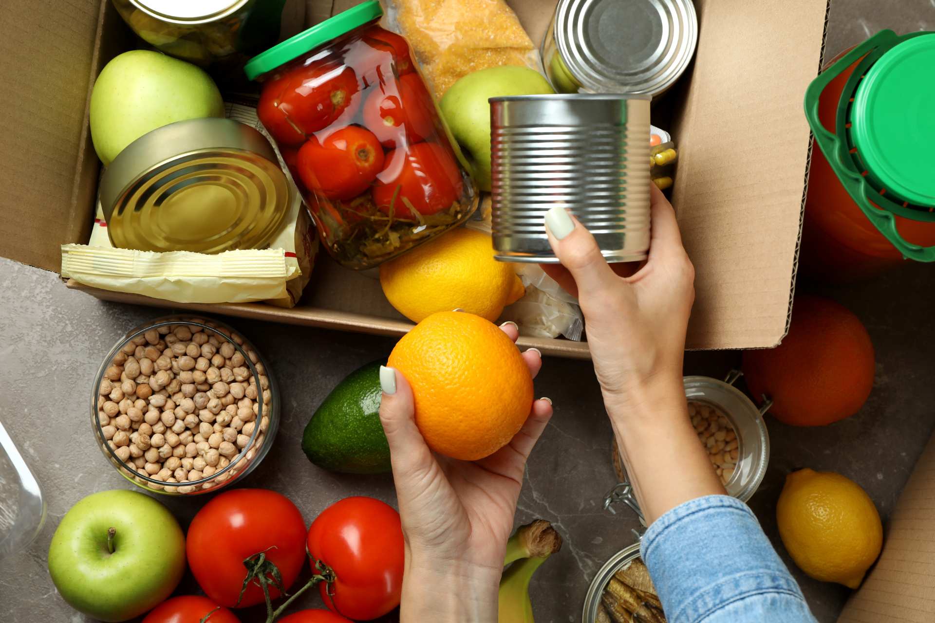 A box filled with cans of food, fruits, and veggies