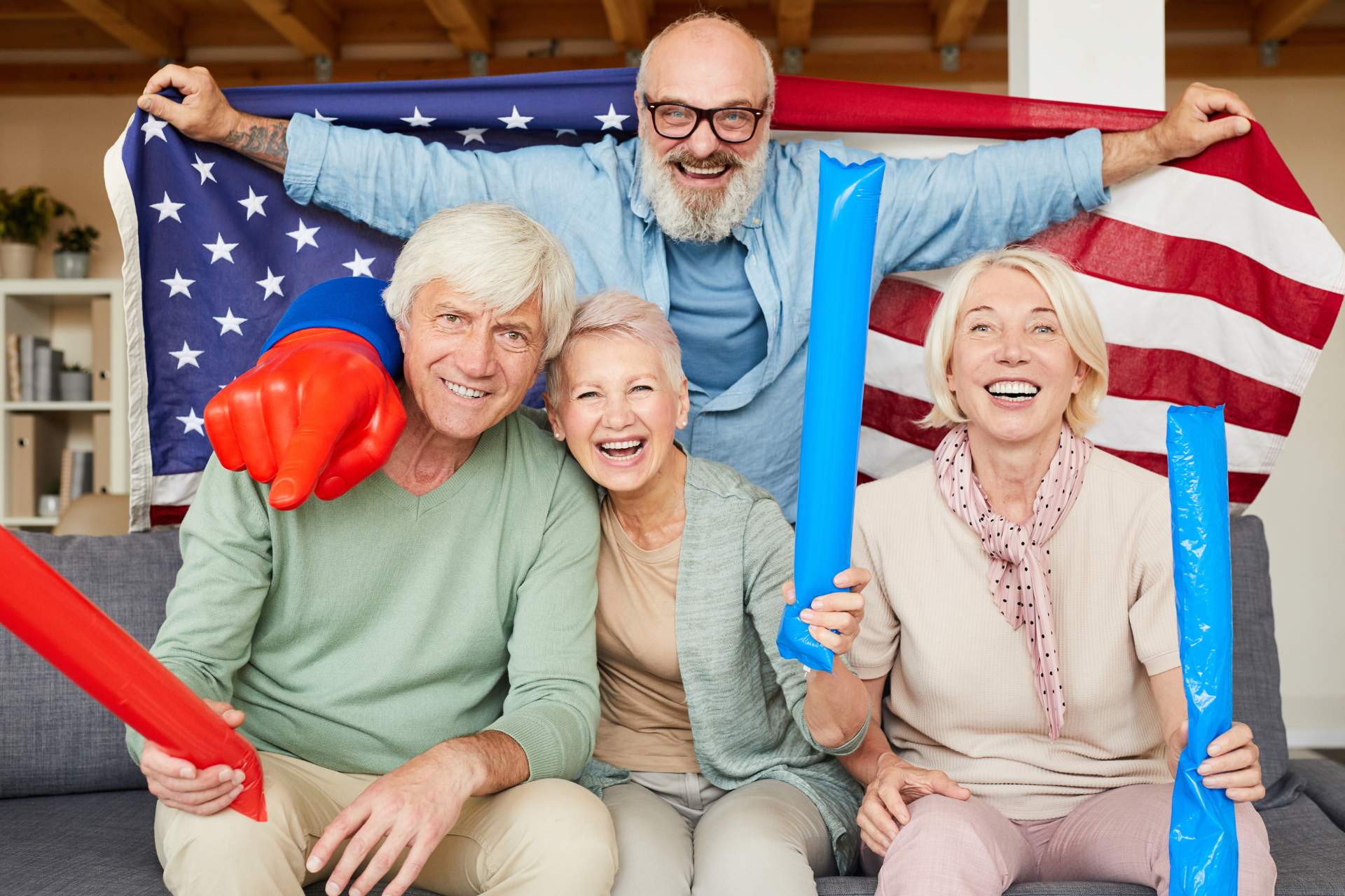 Senior residents celebrating Independence Day with an American flag, patriotic decorations, and festive noisemakers during a community event at an assisted living community.
